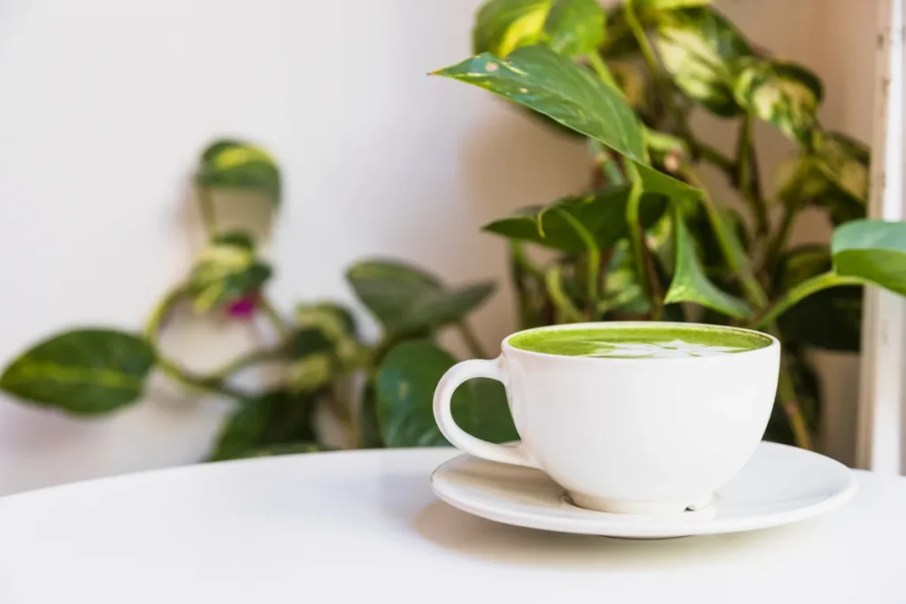 Xícara de porcelana branca contendo café verde sobre uma mesa.