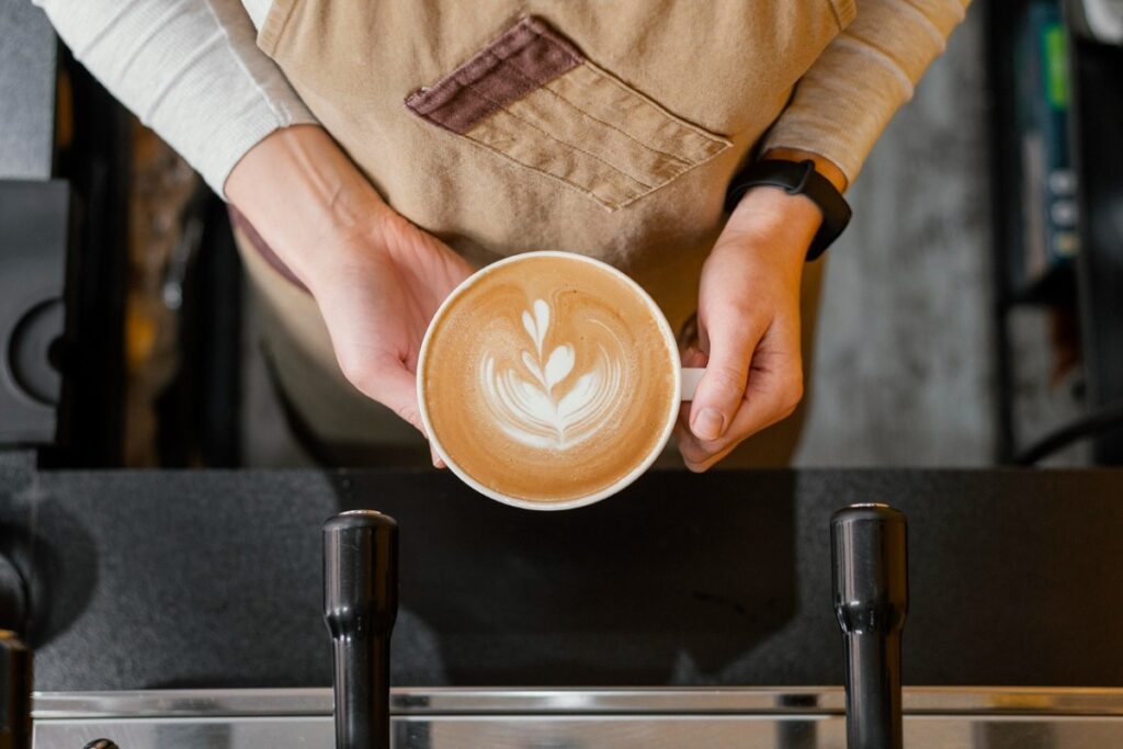 Barista segura xícara de café espresso com leite que formam um belo formato na xícara. A foto foi tirada de cima e foca nas mãos do barista e na xícara com a bebida