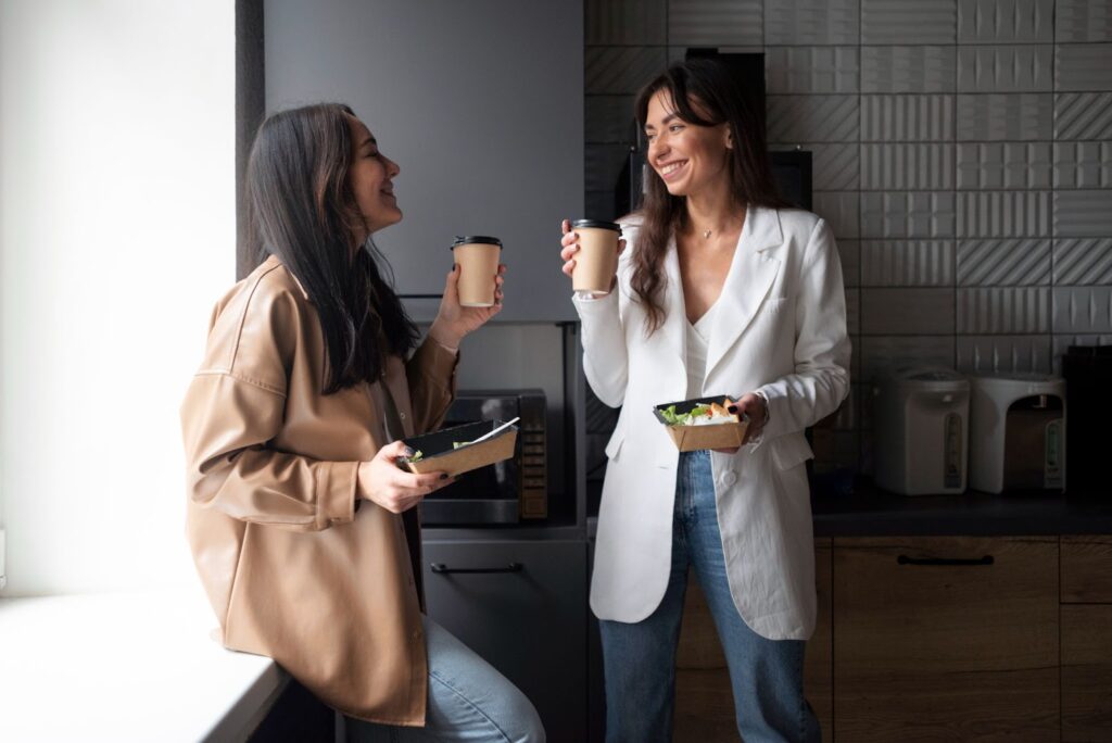 duas mulheres conversando em pé, segurando um copo de café e uma salada