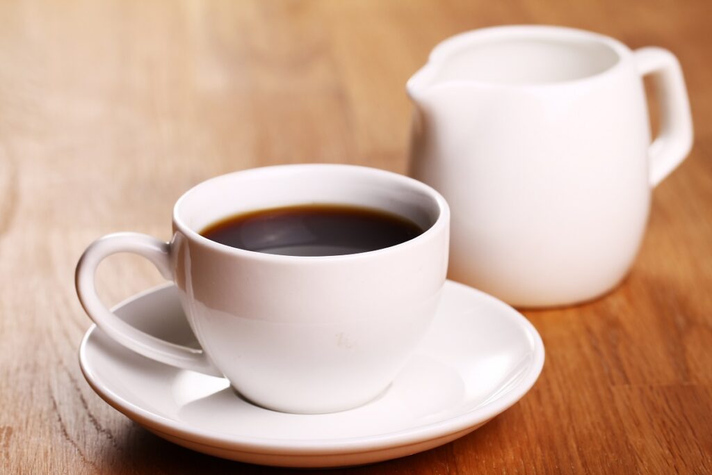Bule de café ao lado de xícara branca de café sobre pires em mesa de madeira.