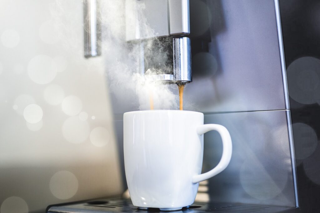 Xícara de café embaixo de máquina que derrama bebida quente na mesma.
