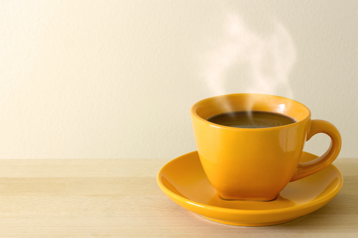 Uma mesa com uma xícara e um pires amarelo sobre ela. Dentro da xícara, café quente com fumaça saindo.