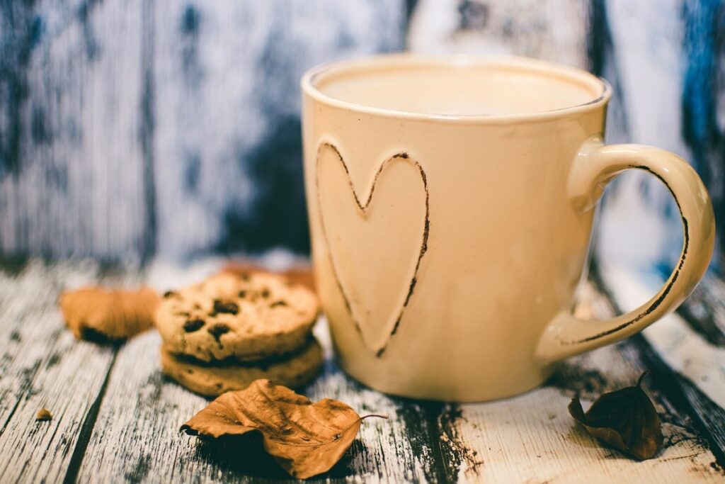 Cookies e xícara marrom com café e folhas secas ao redor em mesa de madeira