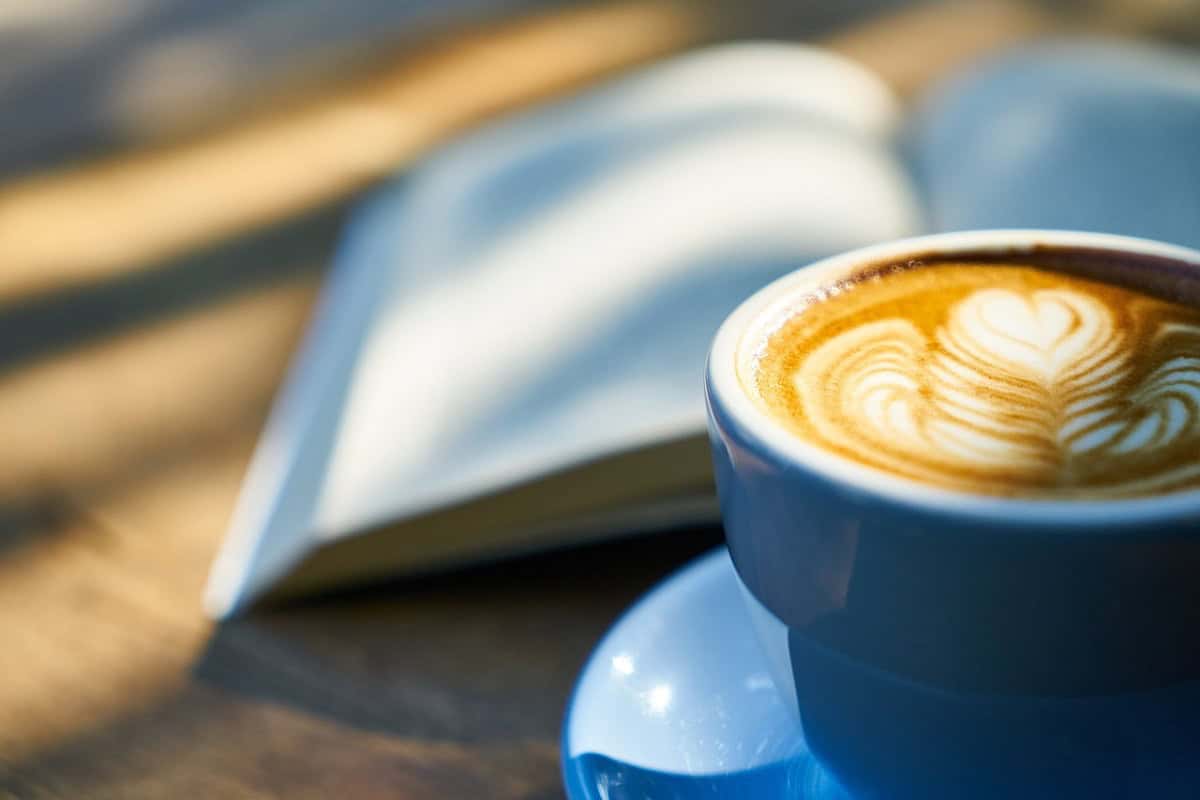 Xícara de café em foco diante de livro sobre mesa de madeira