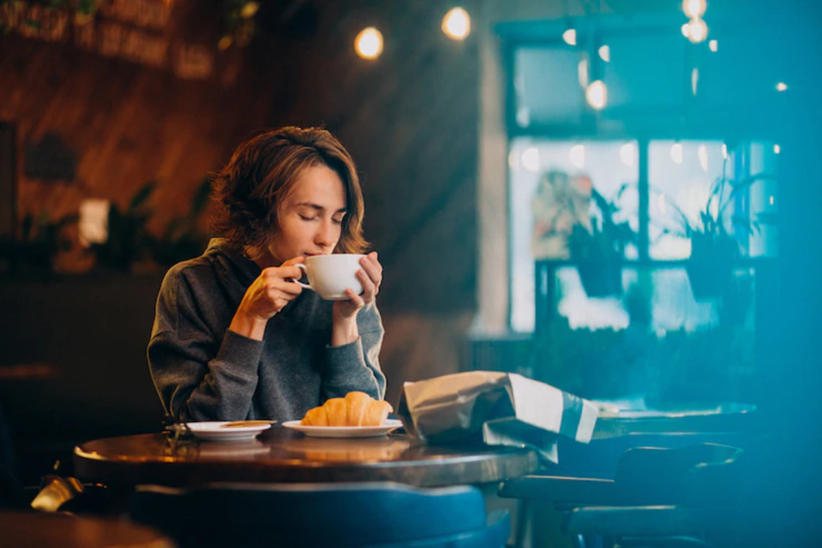 Mulher bebendo café e comendo croissant em mesa de restaurante rústico