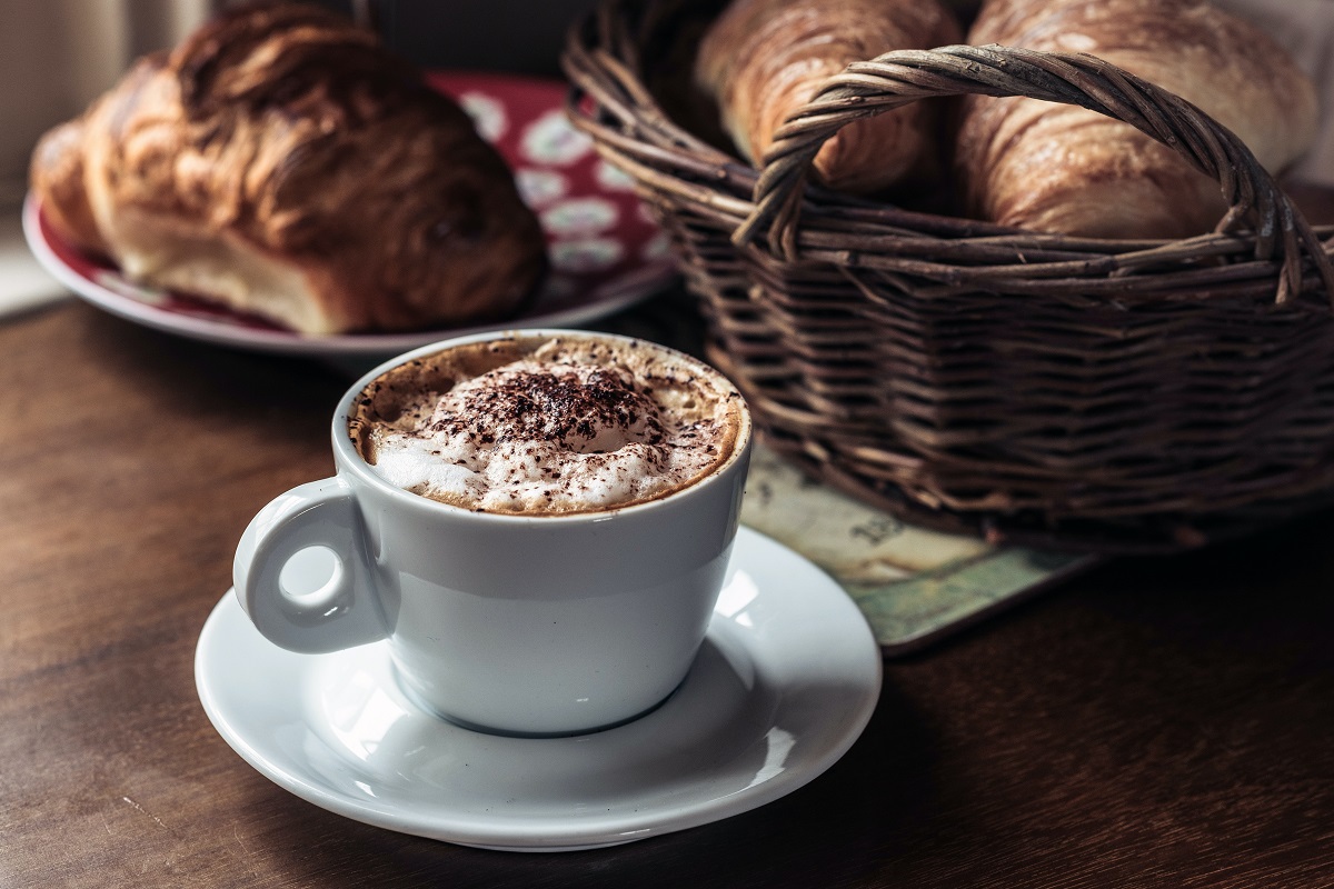 Xícara de café de cápsulas diante de dois cestos de pão de madeira em mesa de madeira