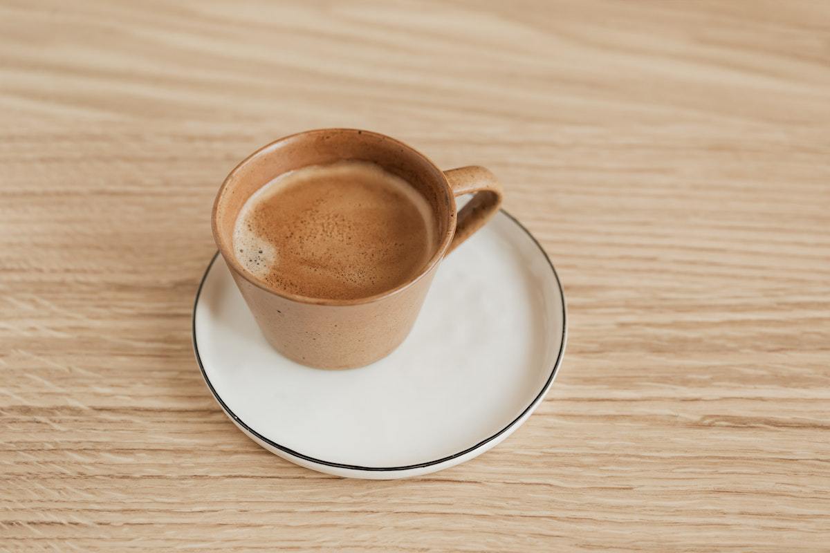 Xícara de café em creme de cor marrom sobre pires e em mesa de madeira
