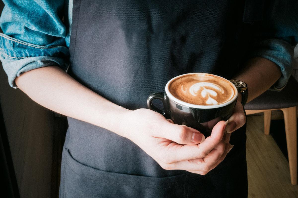 Barista segurando café espresso com detalhes de corações feitos com leite na bebida