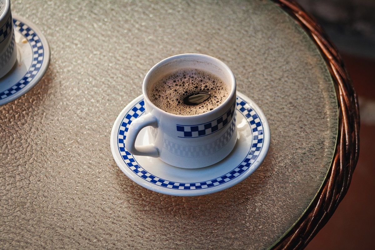 Xícara de café em cima de mesa redonda de vidro com pires branco abaixo do mesmo