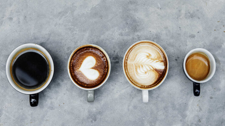 Quatro tipos de xícara diferentes com quatro tipos de café, cada um com um desenho diferente, sobre mesa cinzenta de pedra