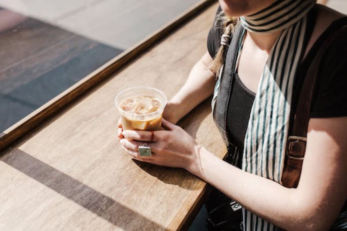 Mulher segurando copo com bebida a base de café sobre balcão de madeira