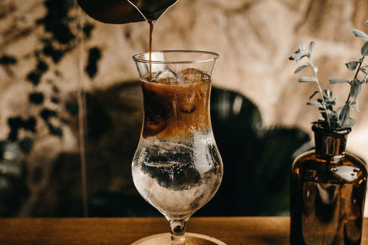 Bebida à base de café sobre balcão de madeira com pessoa jogando mais café na taça