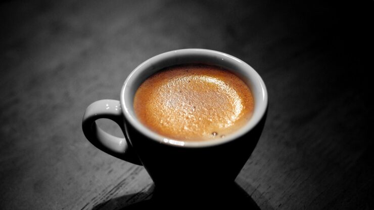 Xícara com bebida sobre mesa de madeira cinzenta em ambiente escuro representando o tema Perguntas sobre café espresso