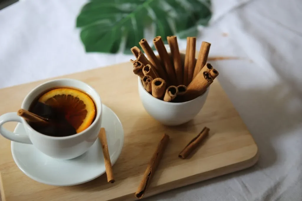 Xícara de chá com canela e laranja em uma bandeja de madeira.