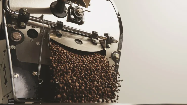 Máquina de torrefação liberando grãos de café torrados em um recipiente, destacando o processo industrial de produção.