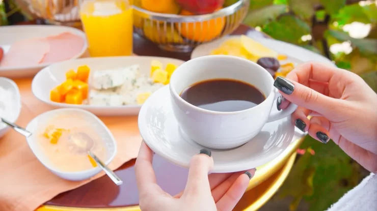 Mesa com café preto, frutas frescas, queijos, suco de laranja e pratos sofisticados em ambiente ao ar livre.