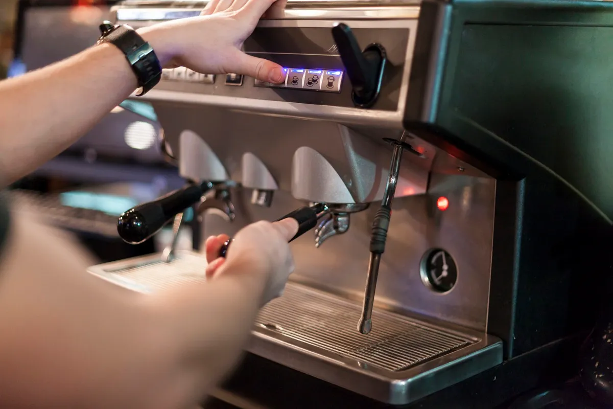 Barista operando máquina de café expresso profissional em aço inoxidável com funções avançadas.