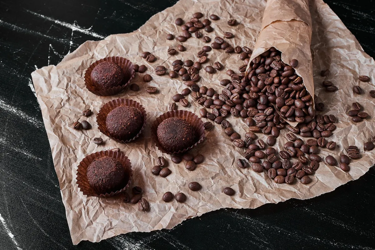 Bombons artesanais de café sobre papel pardo, acompanhados de grãos de café espalhados ao redor.