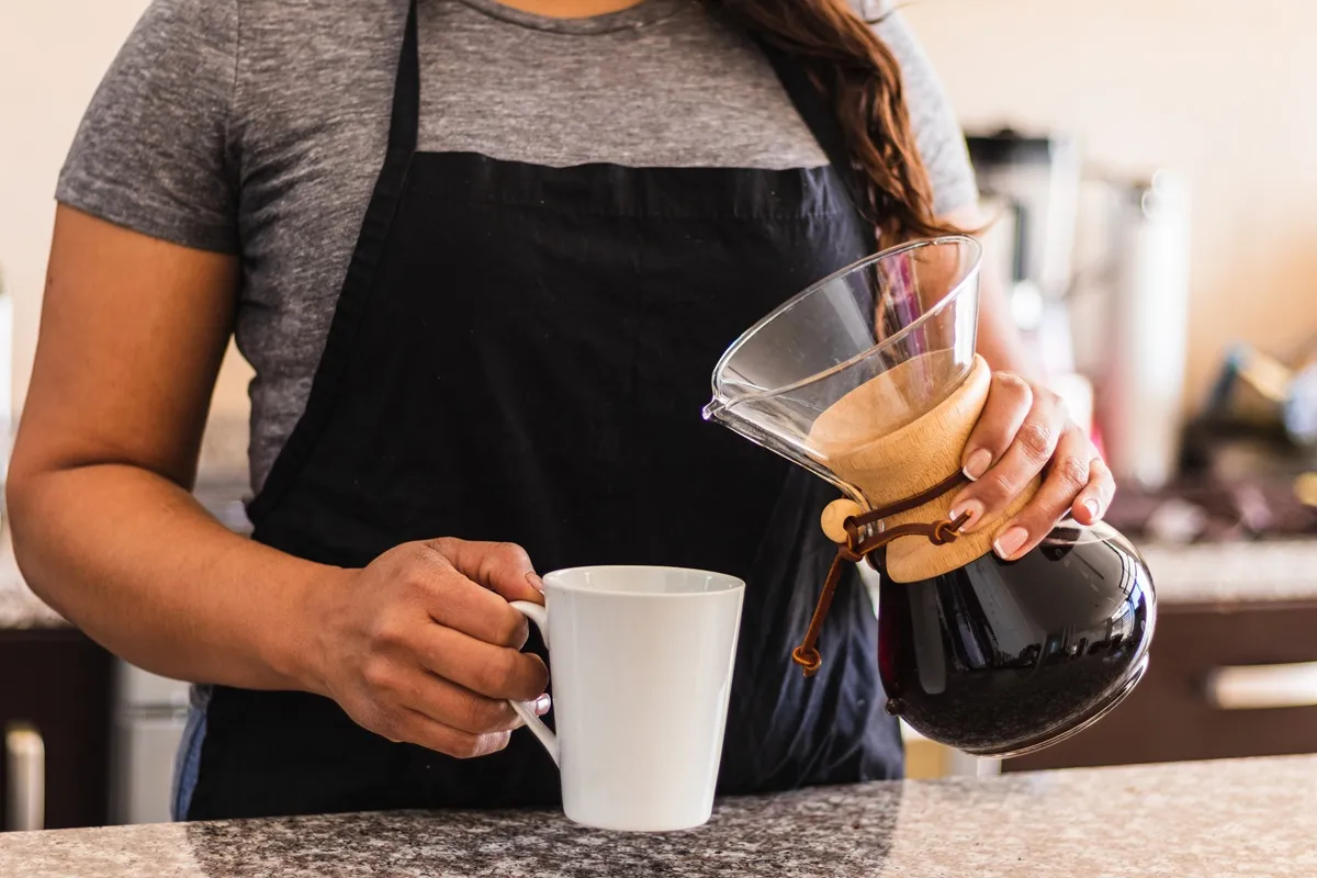 Barista servindo café filtrado em uma xícara branca utilizando uma Chemex, método de preparo artesanal.
