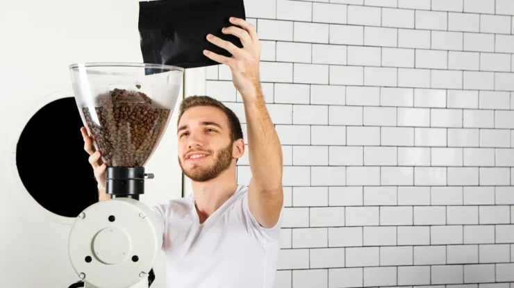 Barista despejando grãos de café em um moedor industrial para preparo artesanal.