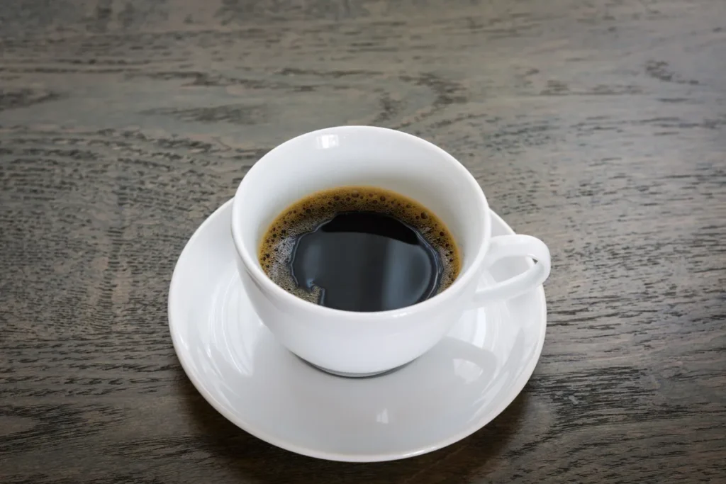 Xícara branca de café preto sobre mesa de madeira escura, representando a principal fonte de cafeína para energia e foco.