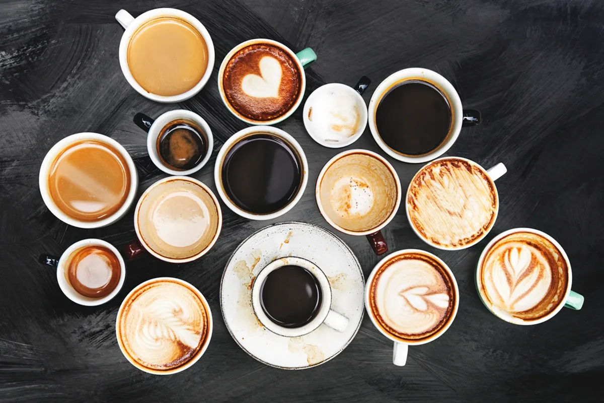 Vista aérea de várias xícaras de café sobre uma superfície escura, apresentando diferentes tipos de preparo, incluindo expressos, cappuccinos e cafés com latte art.