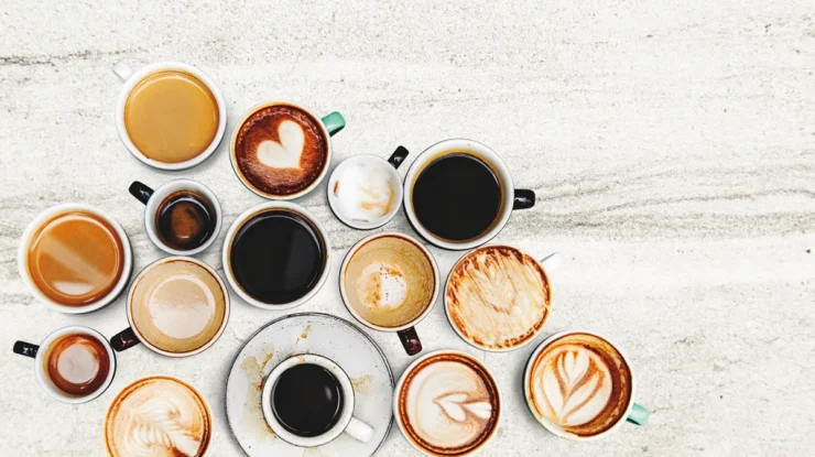 Vista aérea de diversas xícaras de café com diferentes tipos de preparo, incluindo expressos, cappuccinos e cafés com arte em leite vaporizado.