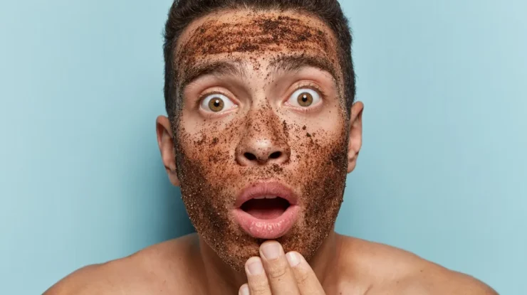 Homem surpreso com máscara esfoliante de café no rosto, expressando espanto enquanto toca o queixo.