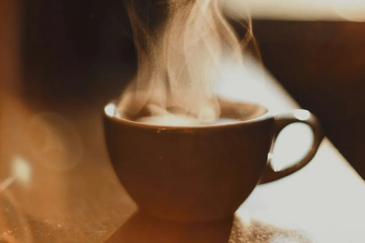 Xícara de café fumegante com vapor subindo, em uma mesa com luz suave
