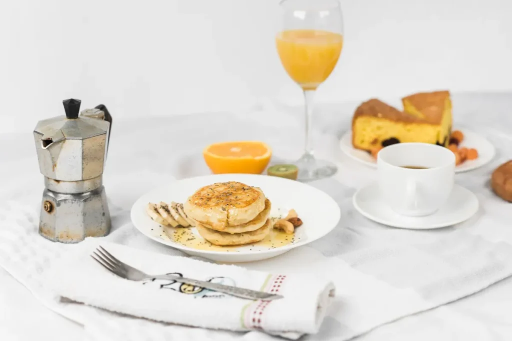 Mesa posta café da manhã com panquecas, bolo de milho e café fresco em cafeteira italiana.