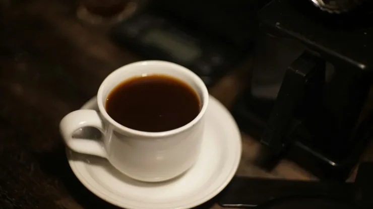 Xícara de café preto em uma bandeja, com um fundo suave e objetos de café ao redor.