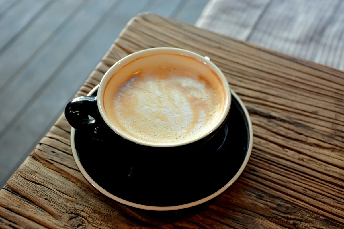 Xícara preta com café cremoso sobre pires preto, apoiada em mesa de madeira com textura rústica
