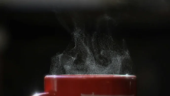 Vapor subindo de uma xícara vermelha de café quente contra fundo preto