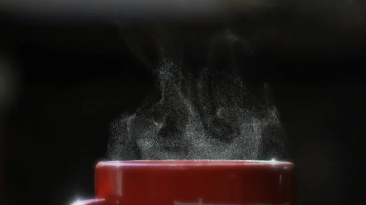 Vapor subindo de uma xícara vermelha de café quente contra fundo preto