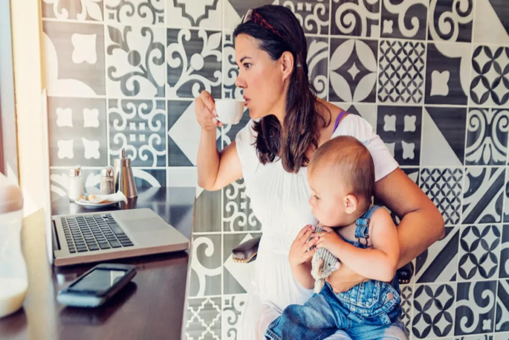Mãe amamentando com um bebê no colo, tomando café e usando o notebook em um café.