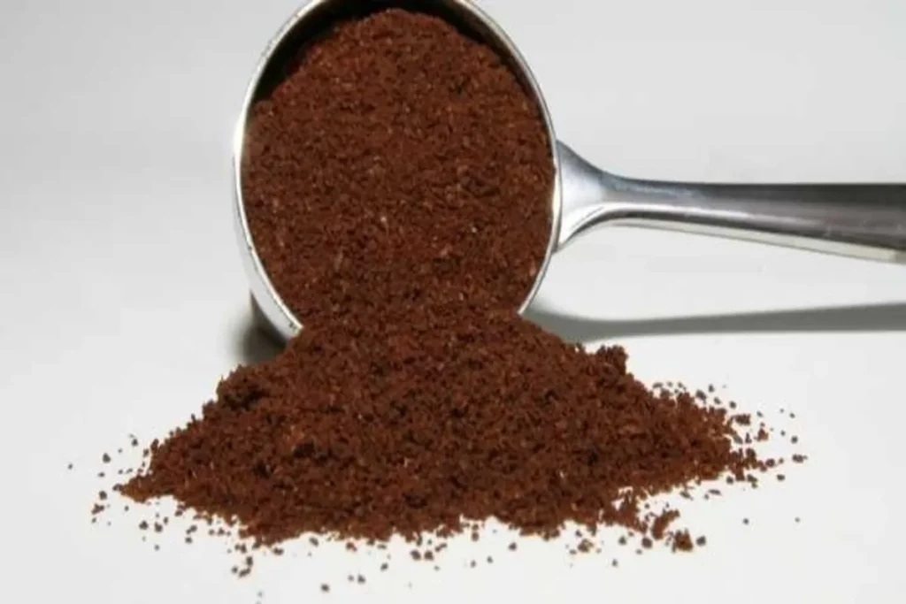 Colher de medida cheia de pó de café moído e uma pilha de café ao lado, indicando a preparação para defumação com café.