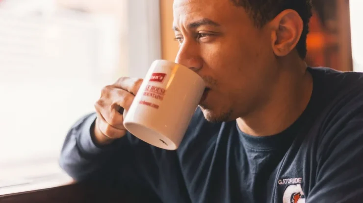 Homem pensativo bebendo café em caneca branca, desfrutando seu horário do café.