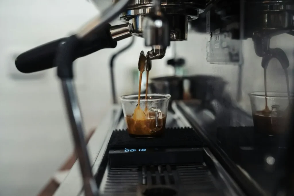 Close-up de uma máquina de café expresso industrial extraindo duas doses de café cremoso em xícaras de vidro sobre uma balança digital, com foco no processo de preparo.