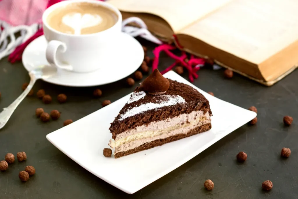Fatia apetitosa de torta de café com cobertura de chocolate e trufa, servida com cappuccino em um ambiente acolhedor com livro aberto e granulados de chocolate.