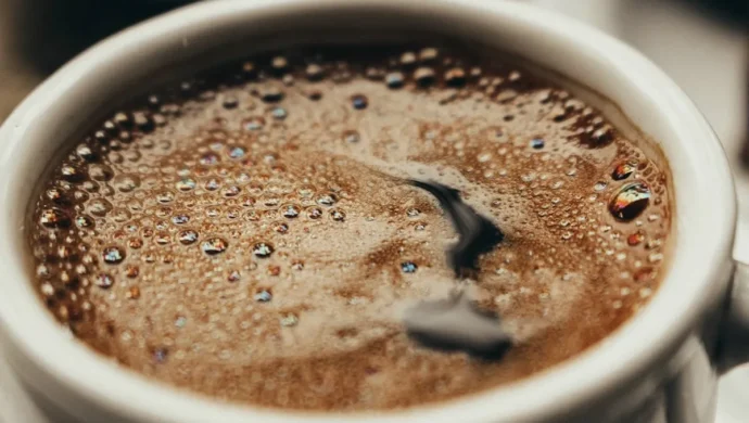 Uma xícara de café preto com espuma e bolhas, focando na superfície da bebida, com a luz criando reflexos coloridos nas bolhas.