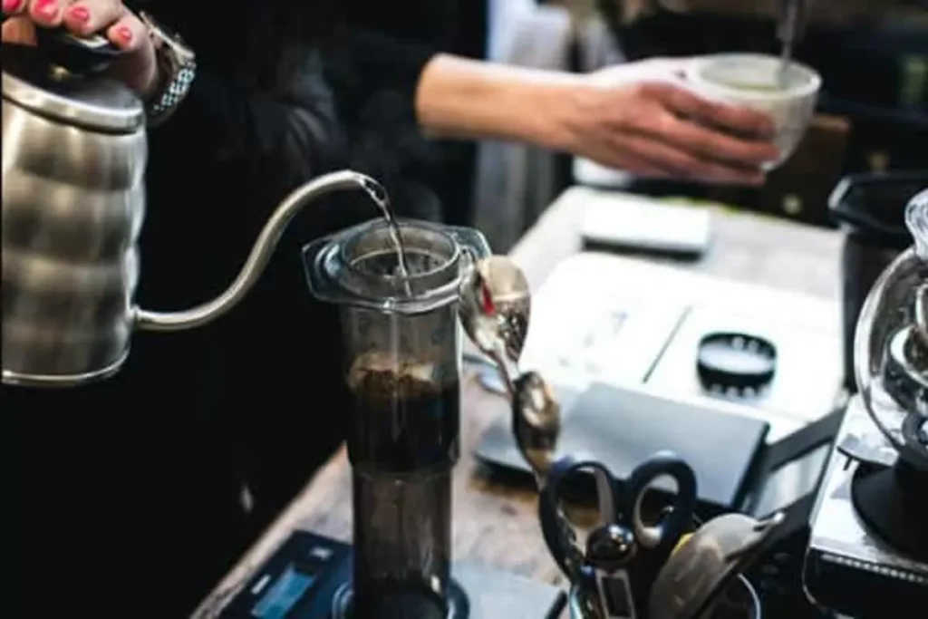 Uma pessoa derrama água quente de uma chaleira de bico de ganso na câmara de um AeroPress para preparar café.
