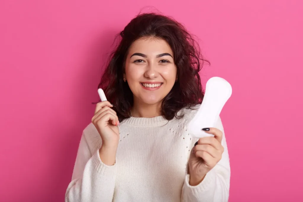 Jovem feliz segurando um absorvente e um tampão, simbolizando a saúde e higiene menstrual.