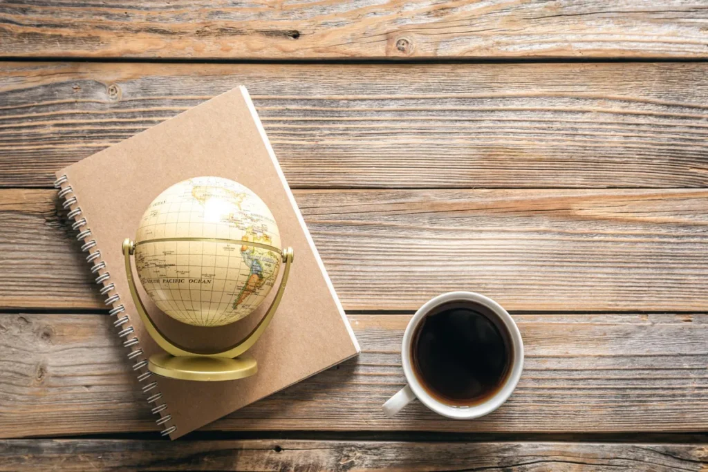 Cup of black coffee on a wooden table beside a notebook and a globe.