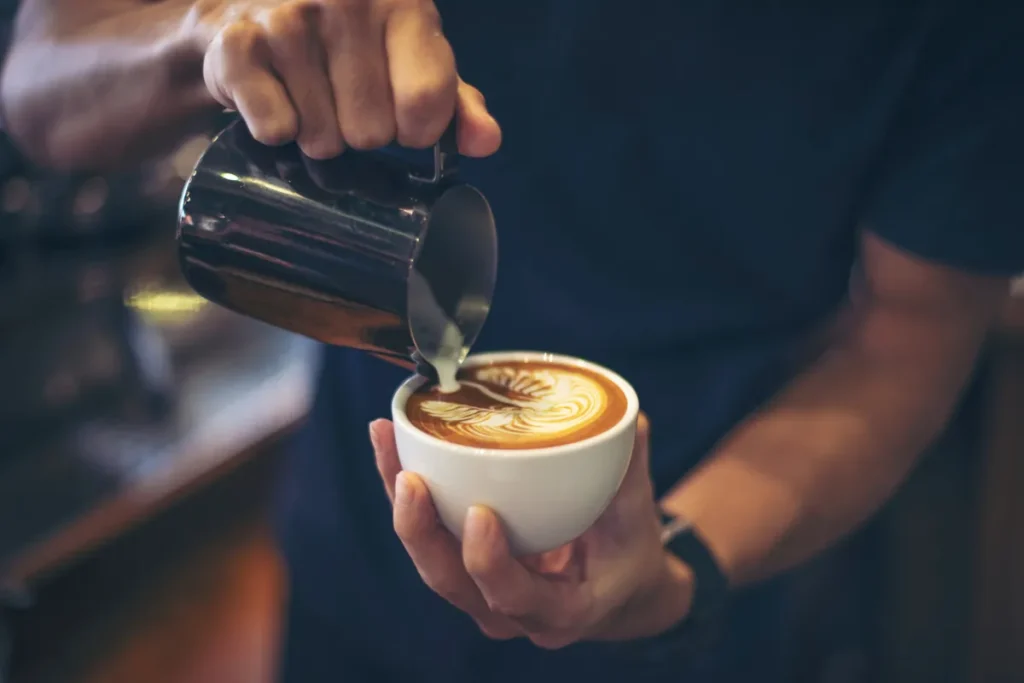 Barista preparando cappuccino com latte art em formato de folha, sabor caramelo salgado.