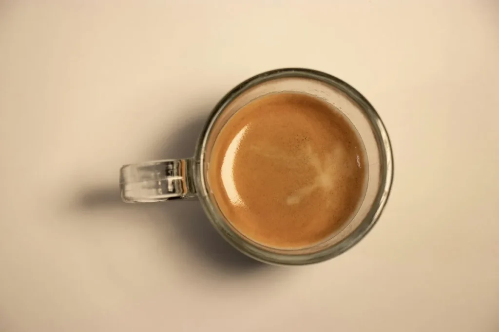 Vista de cima de uma xícara de vidro com café doppio, mostrando a cor e a textura da crema.
