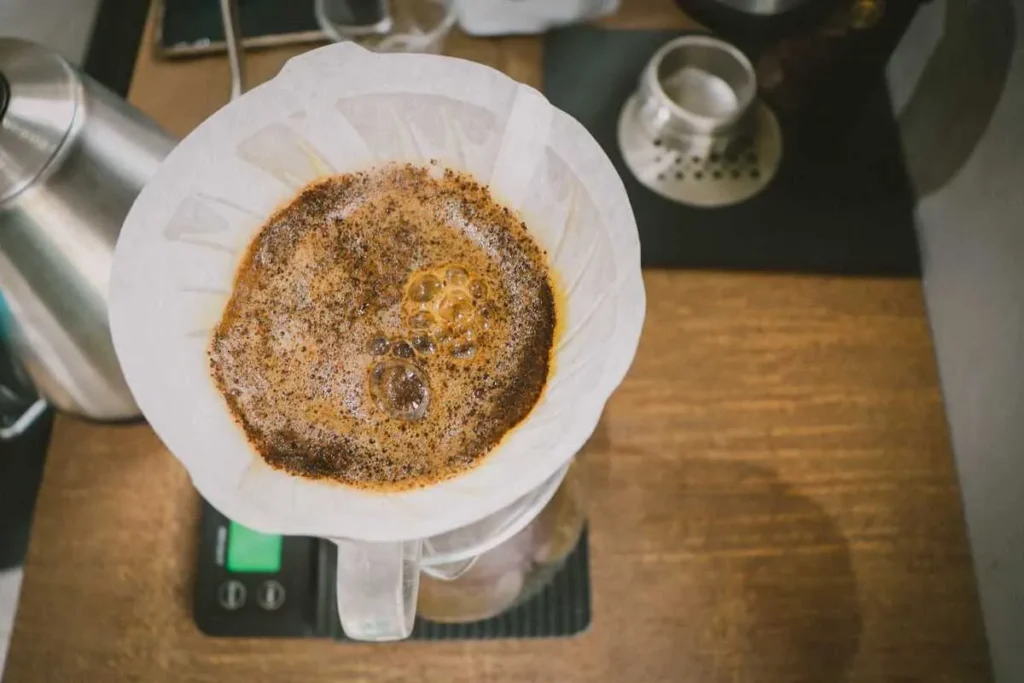 Vista de cima do processo de "blooming" de café, com água quente sendo despejada sobre o pó moído em um filtro, formando bolhas e uma rica camada de espuma.