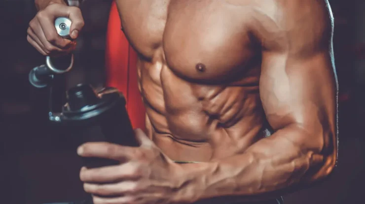 Homem musculoso segurando coqueteleira de suplemento durante treino, representando recuperação muscular.